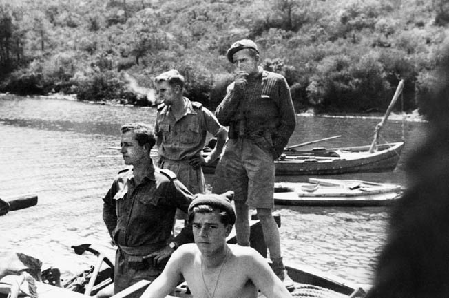 A hero of the SBS, Anders Lassen, who was killed in action late in World War II, stands in the back of a group of his comrades. Several Folboats, the SBS transportation of choice, are seen in the background of this photo.