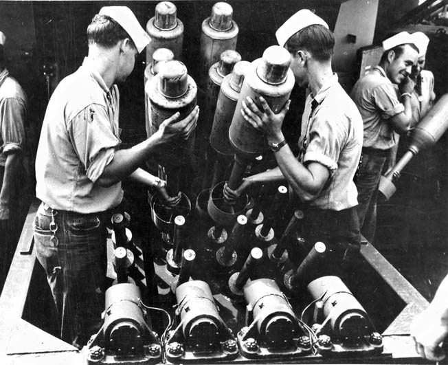 Crewmen aboard a U.S. Navy warship load 24-pound Hedgehog antisubmarine bombs into the projector that was capable of launching them in a circular spread up to 270 yards ahead of the ship. The explosives would detonate only if they struck a target below the surface of the ocean.