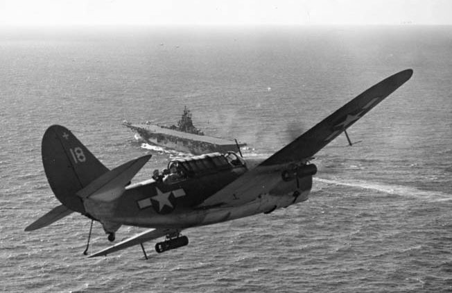 A Curtiss SB2C Helldiver dive bomber approaches a U.S. Navy aircraft carrier. Intended as a replacement for the heralded Douglas Dauntless, the Helldiver proved to be a rugged platform for dive bombing in the Pacific Theater.