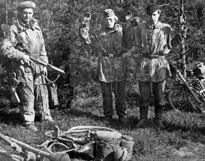 Two members of a Hitler Youth infantry unit trained to attack Allied armored formations stand with their hands up as a British soldier guards them with his Sten gun. The young Nazis were captured while riding bicycles with their Panzerfaust antitank weapons attached. British soldiers were surprised by the youth of many of these combatants.