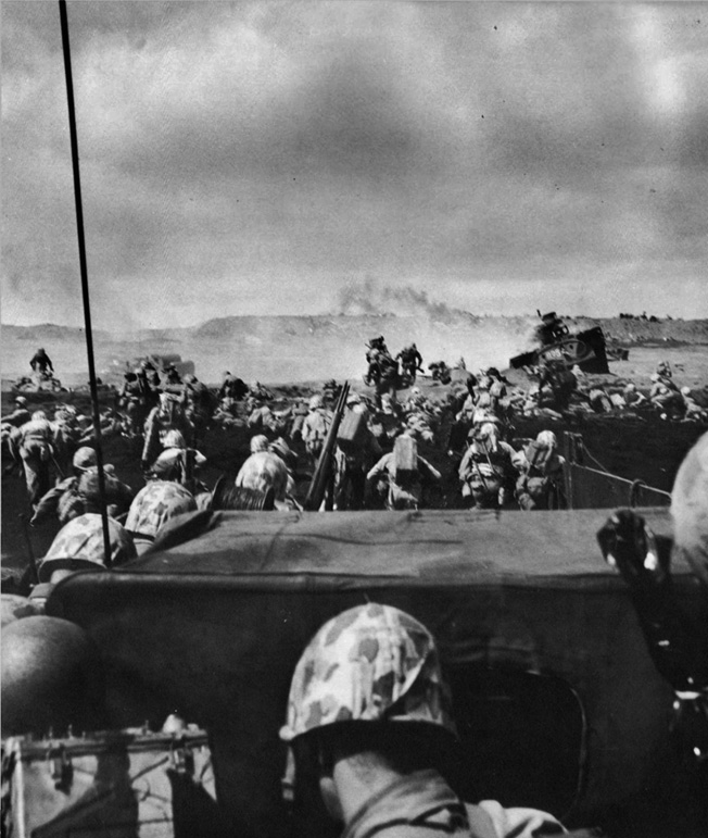 An armored vehicle (right) burns while U.S. Marines hit the black volcanic beach at Iwo Jima, February 19, 1945. Iwo Jima would be the Marines’ bloodiest battle of the entire war. 