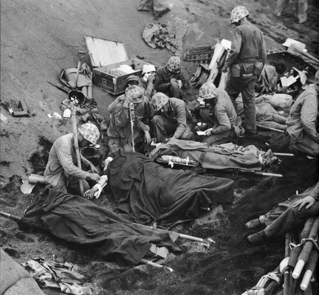 Navy Chaplain Lt. (j.g.) John H. Galbreath (right center) kneels beside a badly burned Marine as Navy doctors and corpsmen administer to the wounded at a makeshift Iwo Jima aid station, February 20, 1945. 