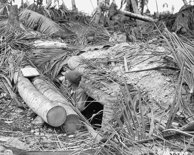 After its original occupants have been killed, an American soldier stands in the entrance to a Japanese bunker on Butaritari. Heavy coconut logs that were used to reinforce the enemy strongpoint.