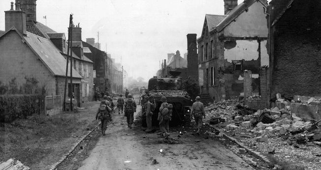 An M4 “Sherman” medium tank from the 3rd Armored Division rolls cautiously through a shattered German village. 