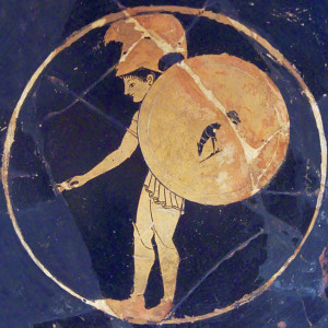 A Savage hoplite flourishes a shield decorated improbably with the drawing of a dog.
