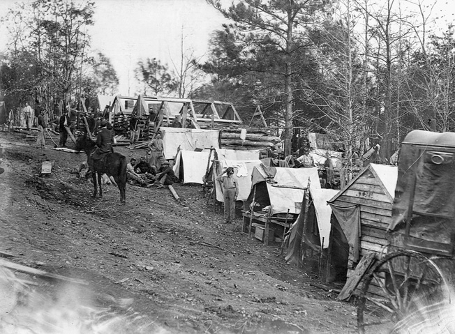 Soldiers construct log huts from nearby trees.