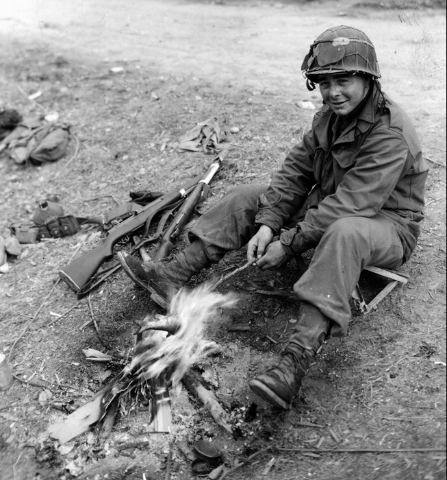 A private with the 42nd Infantry Division cooks a fish over his own personal fire in the Lembach Forest area in France.