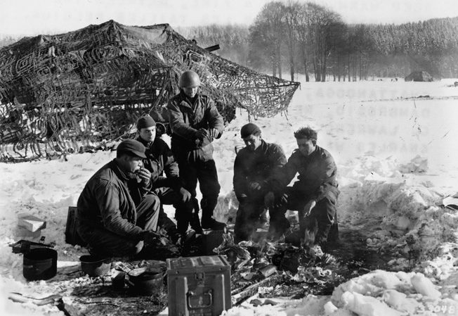 During the closing of the Battle of the Bulge, the crew of a self-propelled 105 with the 2nd Armored Division enjoys a fire and a hot meal outside Les Tailles, Belgium. 