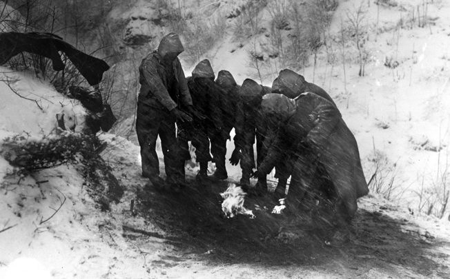 Artillerymen of the 10th Mountain Division huddle around a fire as snow whips around them. Fires were often built on the opposite sides of slopes to hide them from the enemy.