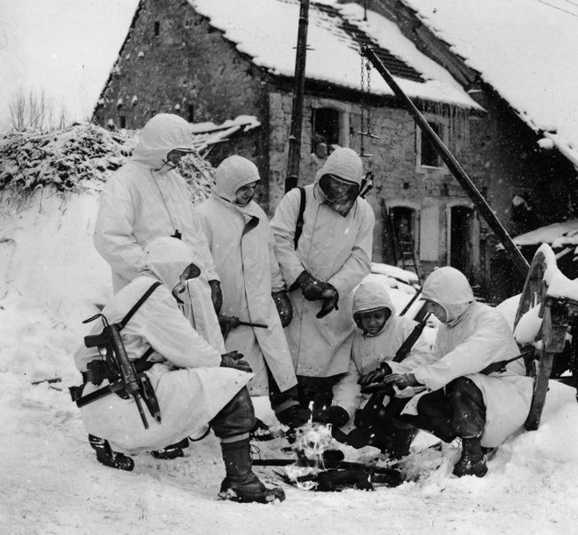 These soldiers, nicknamed “Trouble Shooters,” with the 100th Infantry Division, keep warm over a fire near Butten, France. Two of the soldiers sport M3 Grease Guns.