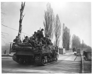 U.S. tanks loaded with infantrymen pass through a final roadblock before crossing the Rhine River.
