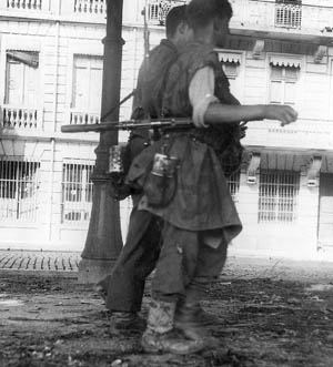During their retreat from Lyon, a pair of German soldiers walk down a desolate city street.