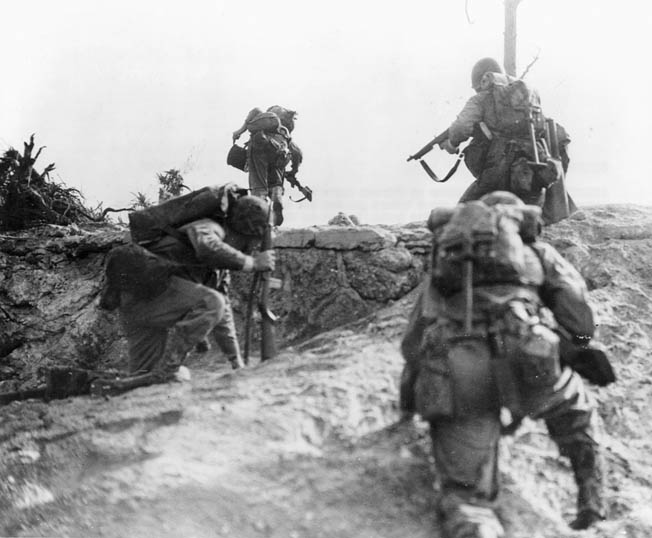 Summoning all their courage, Marines make an uphill assault against the entrenched enemy. A Marine (at left) carries a radio and another a spool of wire