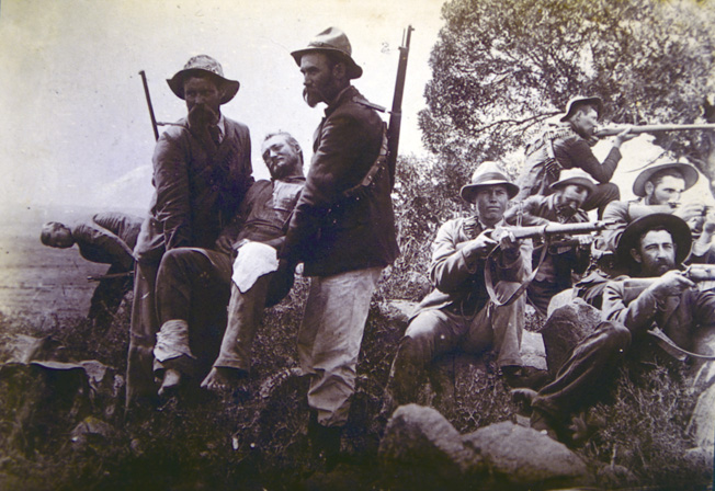 A badly wounded Boer is carried out of danger as his comrades keep watch with their Mausers.
