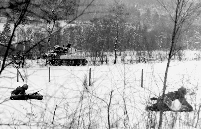 An assault tank rolls past soldiers of the 30th Infantry Division to drop 105mm artillery shells on German positions in Belgium. Miller and his battalion helped the 30th reenter La Gleize.