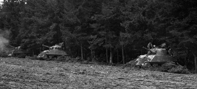 Assault tanks fire a barrage on the enemy from a tree line. Miller could often not see the targets his assault tank was firing on because of Belgium’s dense woods.