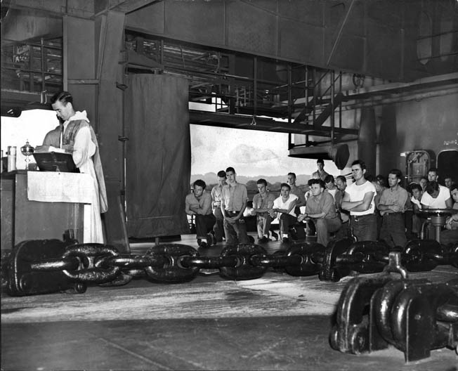 A chaplain conducts Mass aboard the carrier. Ed is to the right in the white T-shirt with arms crossed. 