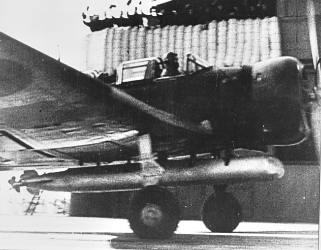 A frame taken from a captured Japanese newsreel showing a Nakajima B5N Kate torpedo plane taking off from an unidentified aircraft carrier. The padding visible on the carrier’s “island” behind the plane are the sailors’ bedrolls.