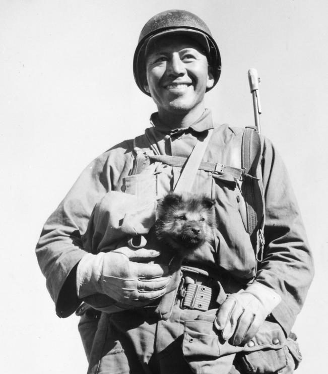 Sgt. Bea Alcoze of Ft. Worth, Texas, carries his canine companion along a hike to a position near Burma Road, as part of the Mars Task Force in Ho-Pong. 