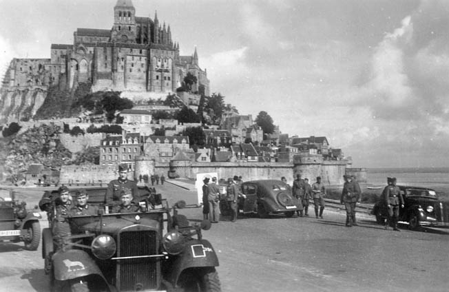 Off-duty Wehrmacht soldiers depart Mont Saint Michel while a French couple opens up their car for inspection. Visits by the French became scarce during the war due to fuel shortages and the special passes needed to move around the country, especially the coast.