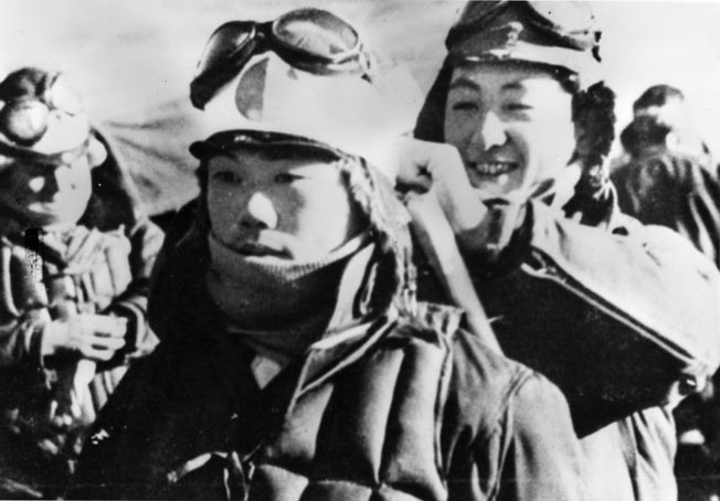A smiling Japanese crewman ties a suicide pilot’s hachimaki (head scarf) to his leather helmet. The symbolic hachimaki was thought to bring the wearer courage.