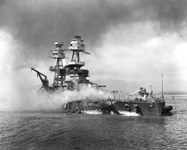 Nevada lies beached and burning at 9:25 am after being hit forward by Japanese bombs and torpedoes. A harbor tugboat is alongside Nevada’s port bow, helping to fight fires on the battleship’s forecastle.