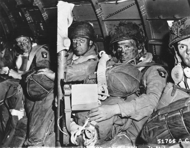 Heavily armed paratroopers of the 101st Airborne Division await the signal to stand up and hook up. Their faces are blacked to camouflage them during the night assault.