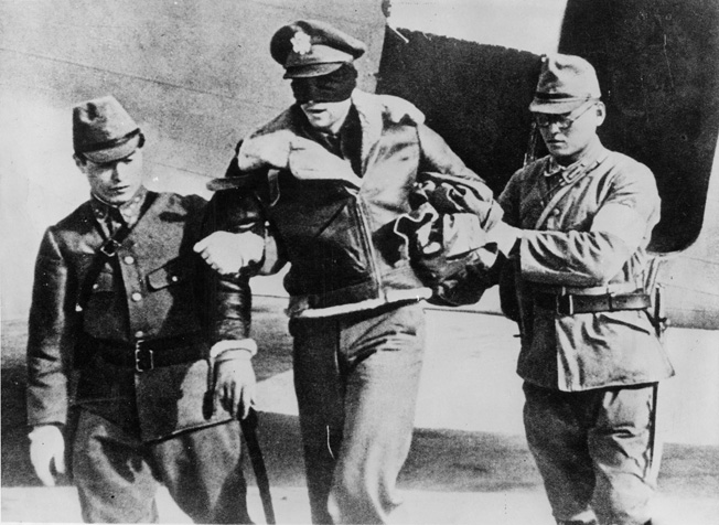 A blindfolded American aviator—perhaps a member of Doolittle’s Raiders—is escorted from a plane by Japanese soldiers. The Japanese stated that any airman shot down over Japan during the raid would be executed.