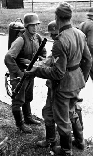 A soldier helps a comrade strap on a flamethrower unit prior to a training exercise.