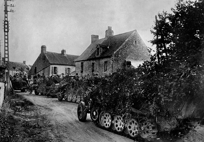 Camouflaged to avoid detection from the air, German SdKfz 7 half-tracked troop carriers move through a French village in hopes of breaking out of the encirclement.