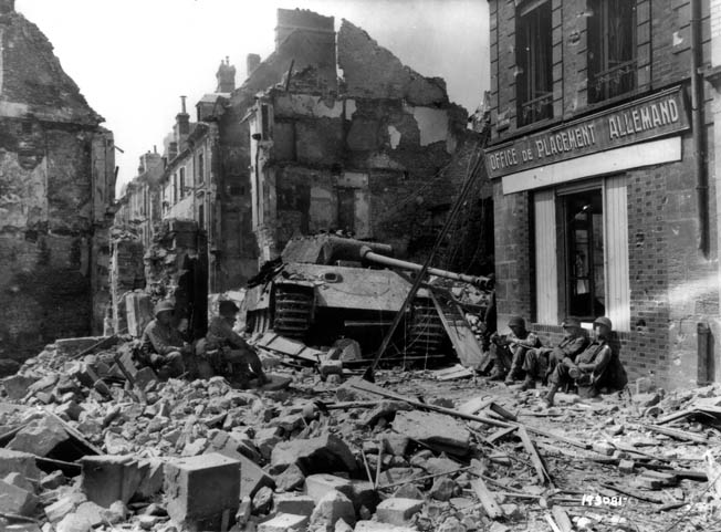 American troops rest in the rubble of Argentan next to a knocked-out Panther medium tank and wonder why their offensive to seal off the enemy escape routes has ground to a halt.