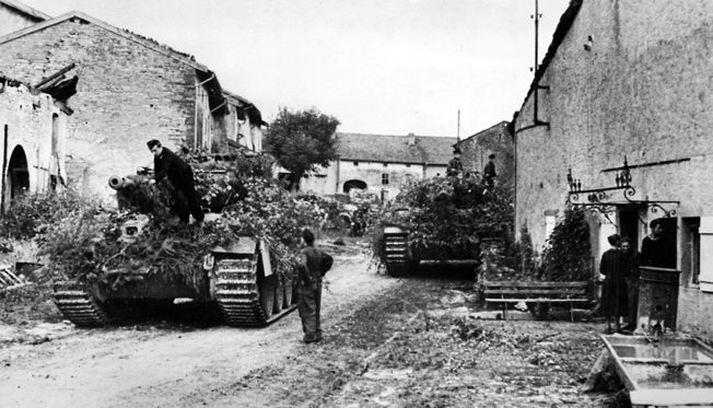 Trying to make their tanks and other vehicles inconspicuous to American aircraft, German troops cover them with tree branches in a town near the Moselle River. 