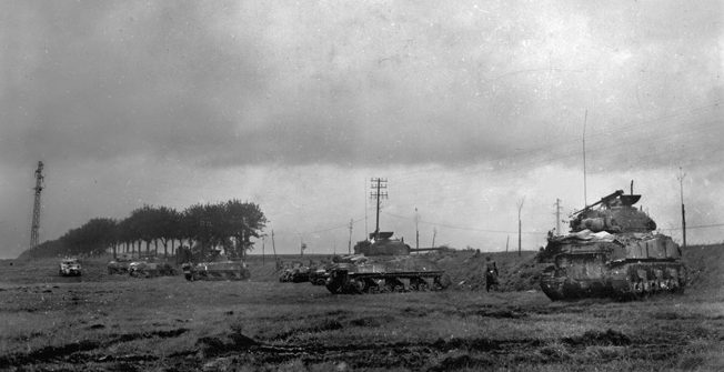 To defend against the more heavily armored German tanks, American armor takes cover behind an embankment near Moncel, France. Overhead, P-47s surprised the German tanks and helped drive them off. 