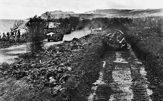 On Saipan a Marine uses a bulldozer to dig a burial trench after the Japanese banzai charge on July 7, 1944. The bodies of some of the 4,000 Japanese killed in the charge lay to the left of the trench. The attackers included walking wounded and men armed with only bayonets tied to wood staffs.