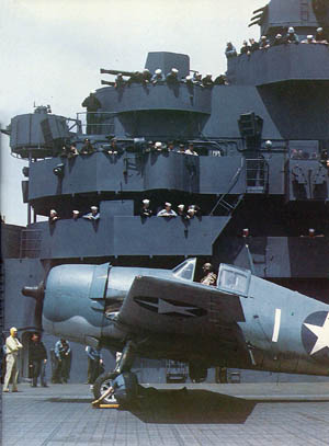 A crewman from the USS Yorktown prepares to remove the wheel chocks of a F6F-3 Hellcat, of the type flown by Crosby, prior to take-off, May 1943.