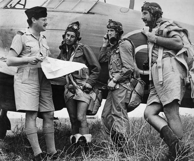 An RNZAF officer briefs a group of pilots standing beside what is possibly a Curtis P-40 Kittyhawk Mk IV fighter. 