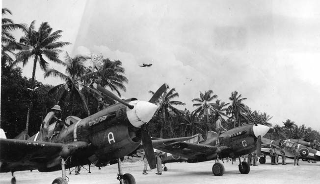 While a Vought F4U Corsair streaks overhead, New Zealand P-40s, provided by the United States, are serviced after returning from a strike on Rabaul in December 1943. The RNZAF got good service out of the obsolescent P-40s.