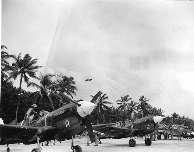 While a Vought F4U Corsair streaks overhead, New Zealand P-40s, provided by the United States, are serviced after returning from a strike on Rabaul in December 1943. The RNZAF got good service out of the obsolescent P-40s.