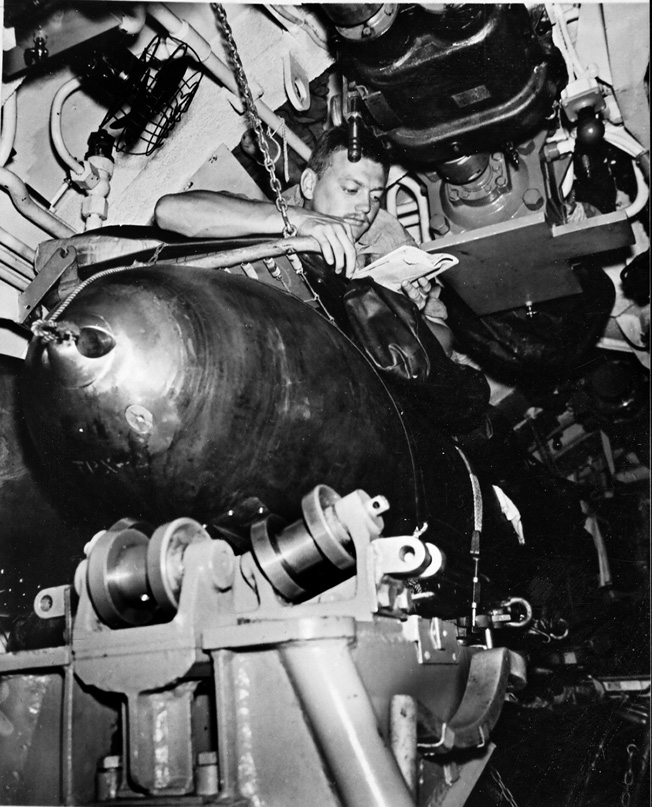 A submarine crewman reads a book in his bunk just a few inches above on the the torpedoes.