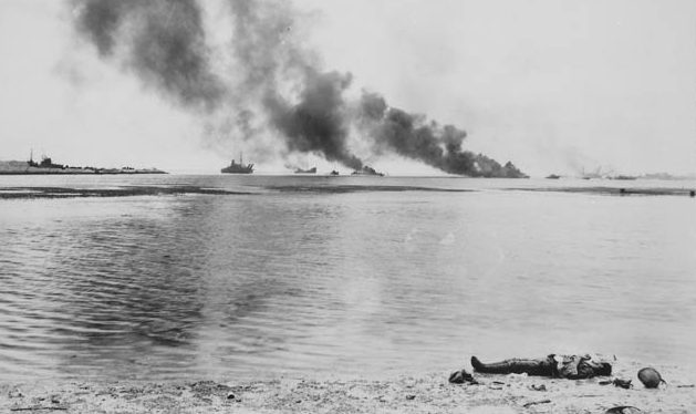 A Japanese soldier lies dead at the water’s edge in Tanapag harbor on the island of Saipan, July 15, 1944. This soldier was among a number of Japanese troops that sought safety aboard ships in the harbor. Several of those vessels were attacked by U.S. aircraft and blaze in the distance.