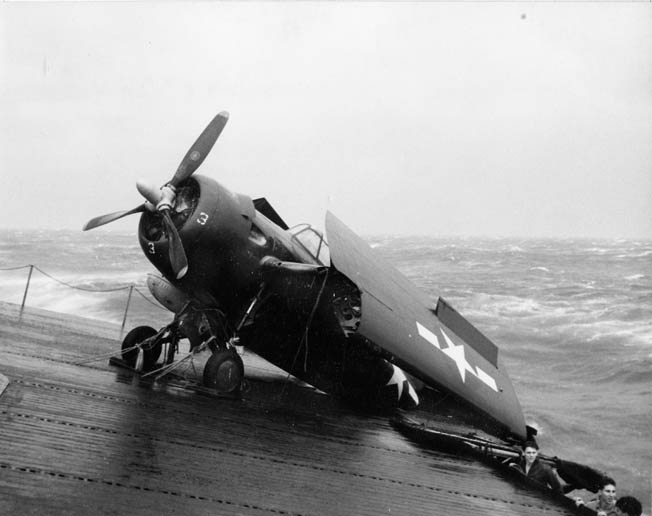 A U.S. Navy FM-2 Wildcat fighter plane hangs off the deck of the escort carrier USS Anzio. Having broken its moorings, the plane was nearly tossed overboard in the raging seas during Typhoon Cobra.