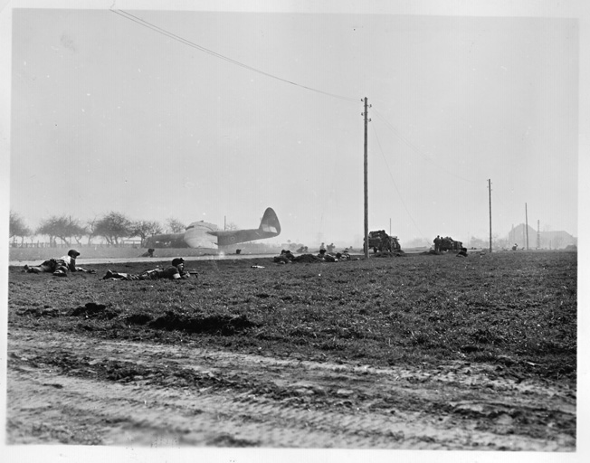 Paratroopers of Colonel James W. Coutts’ 513th PIR hug the ground on Landing Zone “P” as others begin to dig slit trenches along a roadway. A British-made Horsa glider is visible in the distance. 