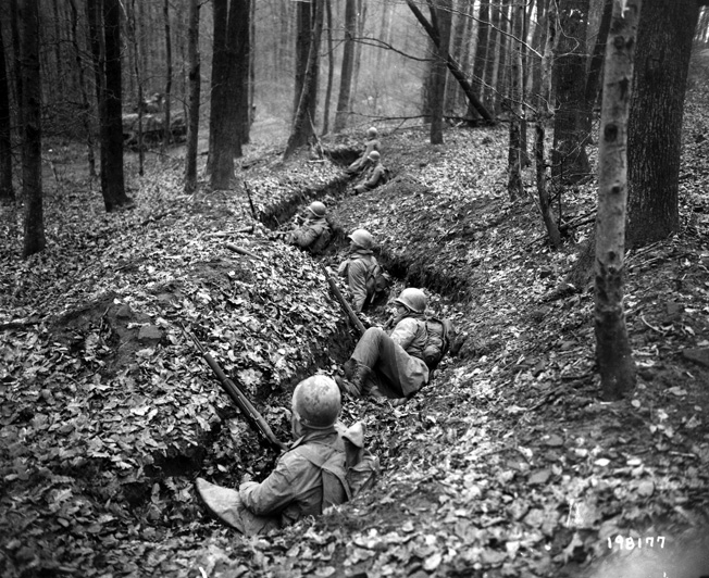 Men of the 399th watch from their trench line as an American tank rolls past on a forest road. By holding firm against the enemy’s counterattacks and capturing Bitche in March 1945, the 100th Division earned praise from higher headquarters.