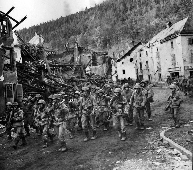 Elements of the 100th Division move through the ruins of Raon L’Etape in the Vosges Mountains area of northeastern France. 