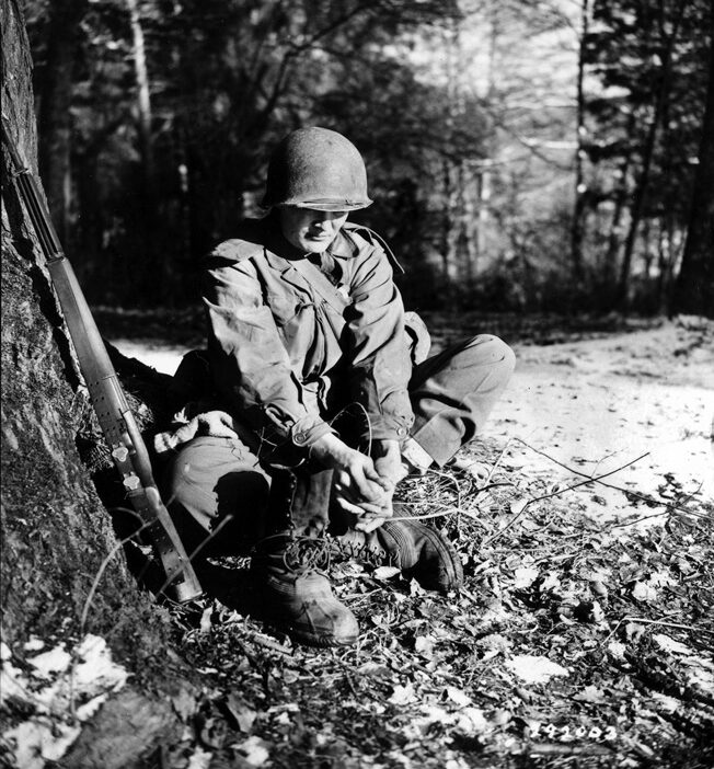 A 399th GI dries his feet and changes socks to avoid trench foot. Officers threatened to court-martial soldiers if they developed trench foot; it was a hollow threat. 