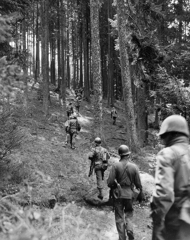 Troops of the 90th Infantry Division move through the woodlands of Czechoslovakia while probing German positions near the southern German-Czech border.