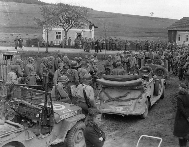 A crowd of 90th and 2nd Infantry Division troops gather as the German 11th Panzer Division makes its formal surrender in May 1945.