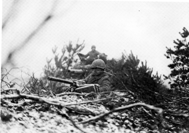 On alert for a coming attack, an engineer holds position with his .30-caliber machine gun near a camouflaged tank.