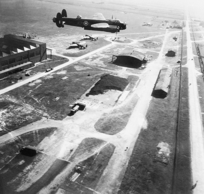 Squadron Leader J.D. Nettleton’s Lancaster bomber flies low over RAF Waddington, Lincolnshire, with its bomb bay doors open. This photo was snapped during practice runs for the Augsburg raid, which occurred three days later. The MAN diesel engine assembly plant at Augsburg was a prime target for RAF bombers since it supplied engines to the German U-boat fleet.