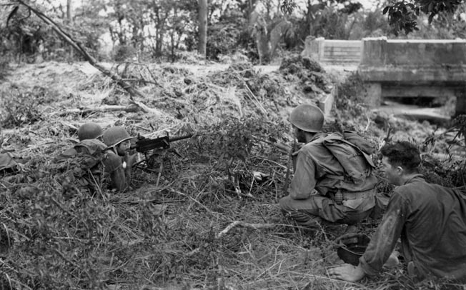 A pair of American soldiers occupy a foxhole with a .30-caliber machine gun at the ready while other members of their squad approach. The sluggish advance against the Japanese on the Bataan Peninsula took its toll on the U.S. troops, while the enemy often fought to the death.